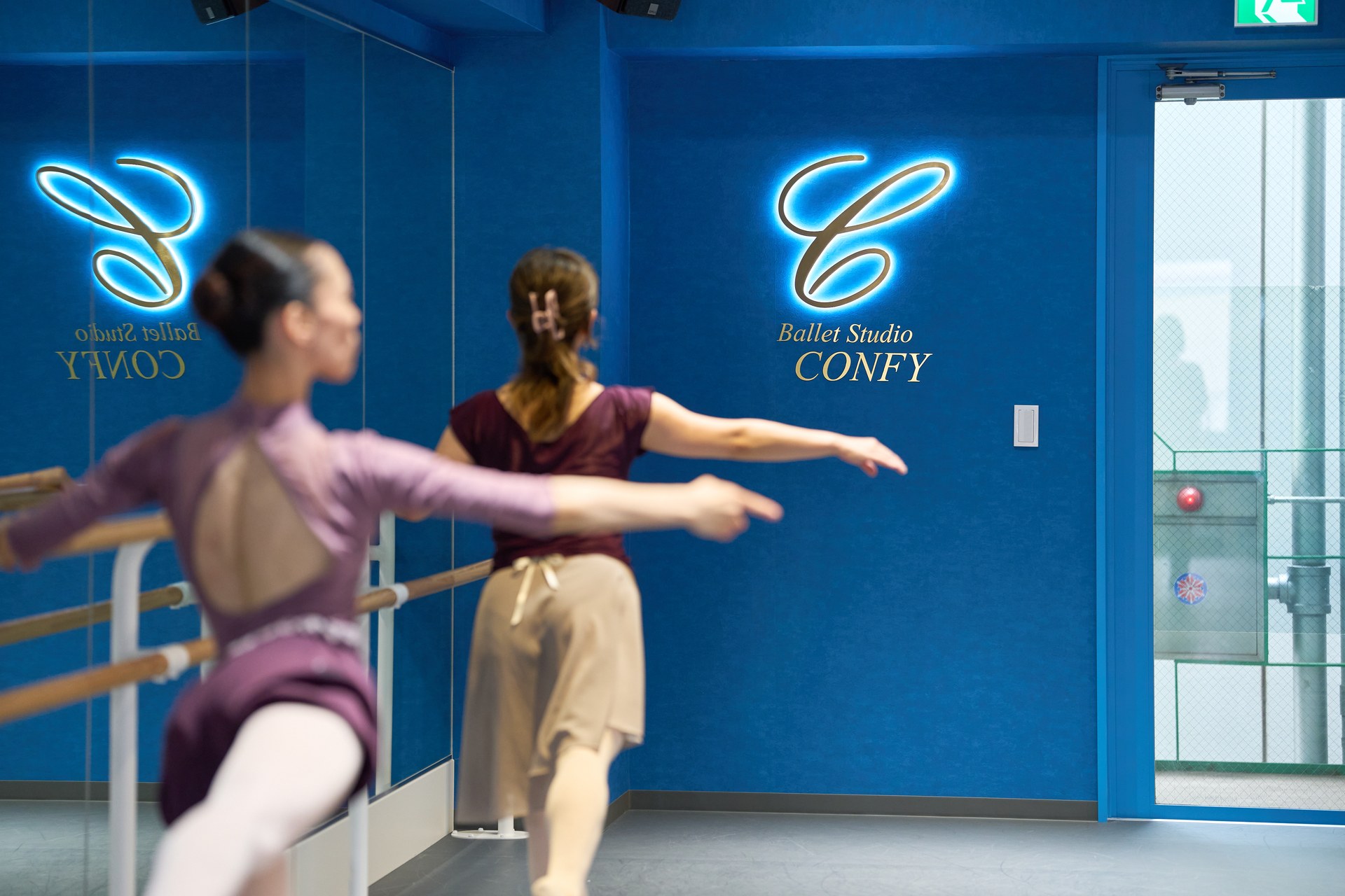 鏡のネオンロゴの前でタンデュをする大人のバレエクラス — 月島 Ballet Studio CONFY